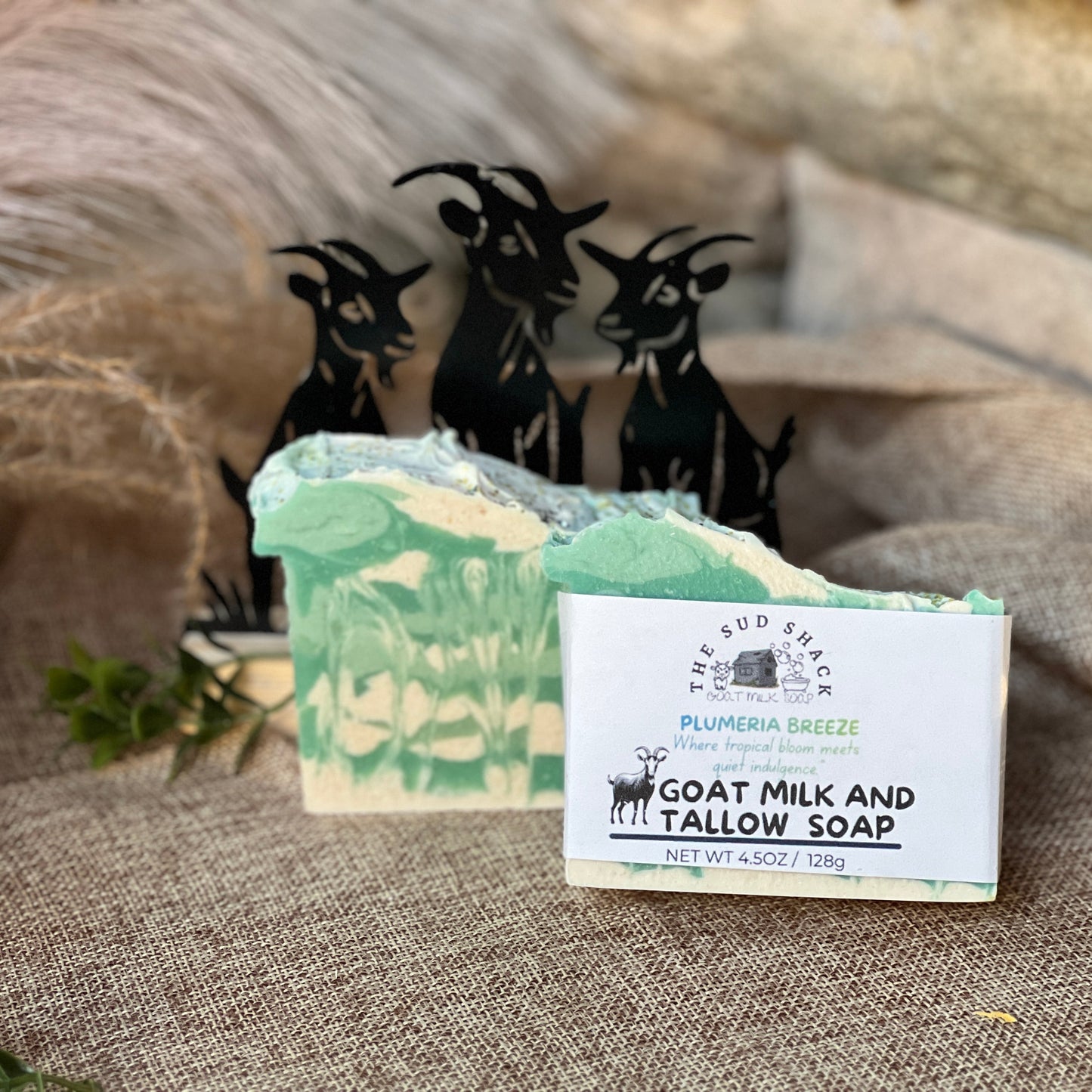 Goat milk and tallow soap with a label on a textured surface, featuring decorative goat figures in the background.