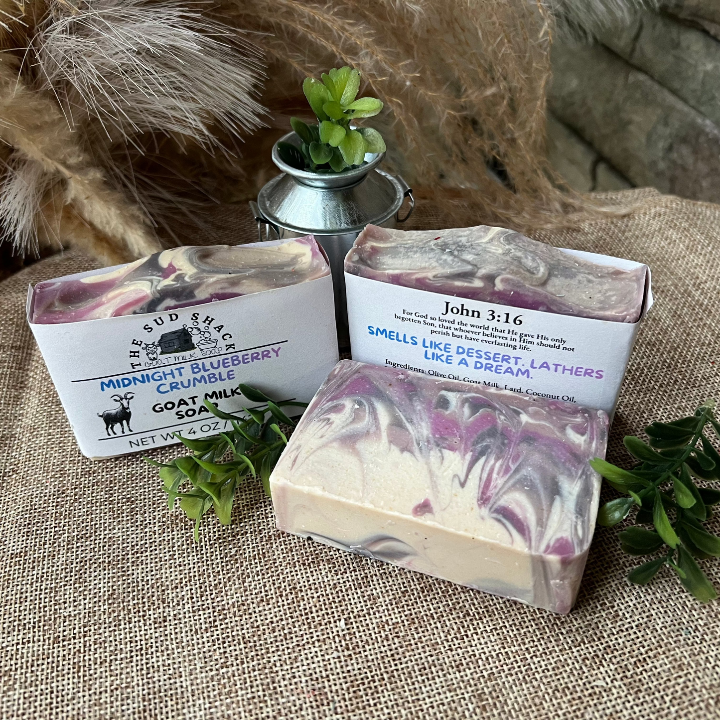 Three bars of soap with packaging on a textured surface with plants.