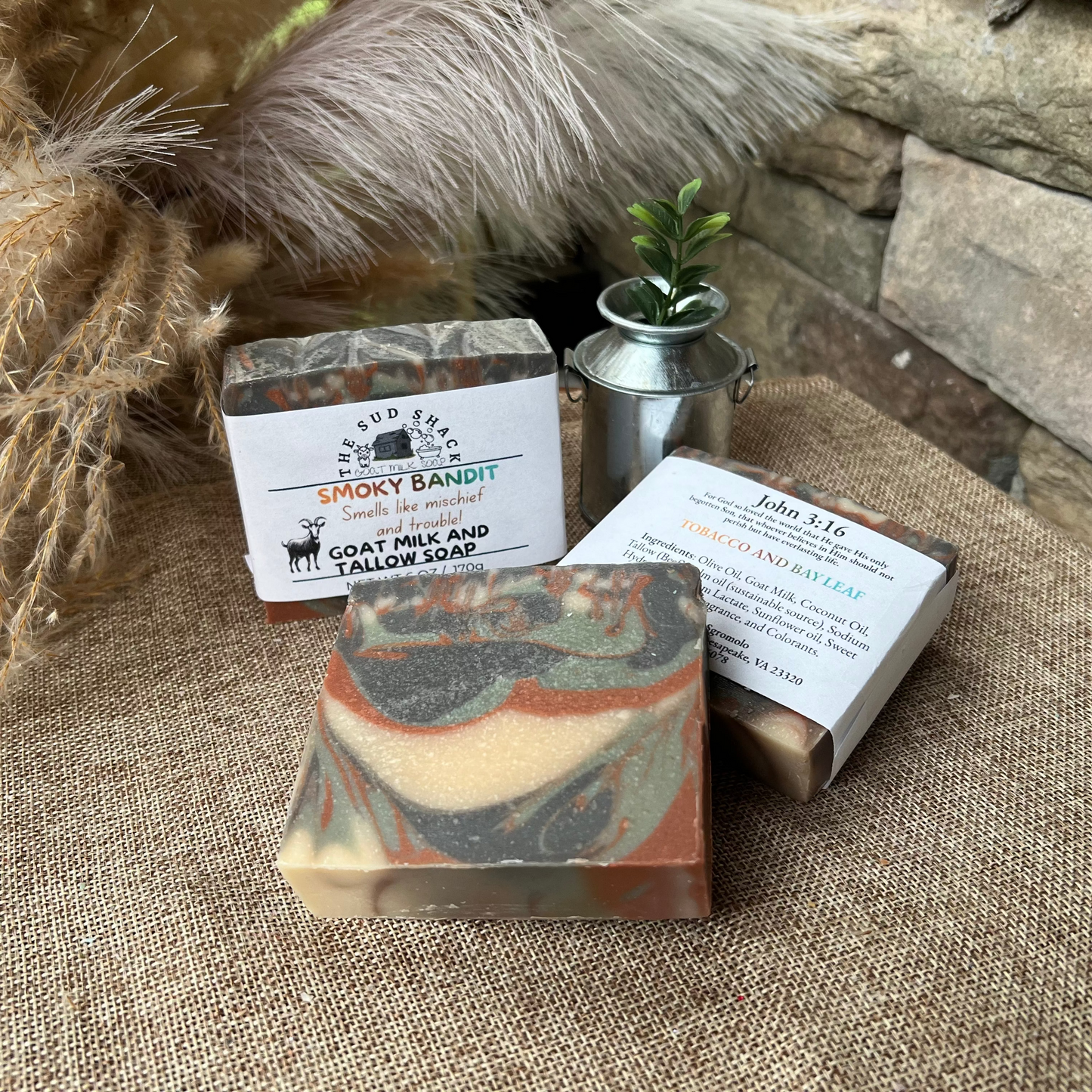 Three bars of soap with labels on a textured surface with natural elements.