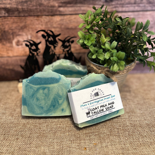 Green soap bar with a label on a textured surface with plants and figurines in the background