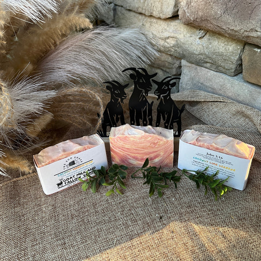 Three bars of soap with decorative packaging on a textured surface with a stone wall background.
