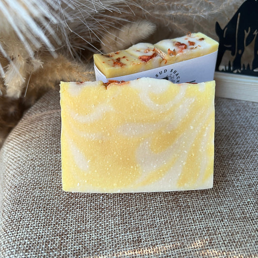 Yellow and white swirled soap bar with a visible brand name on a textured surface.