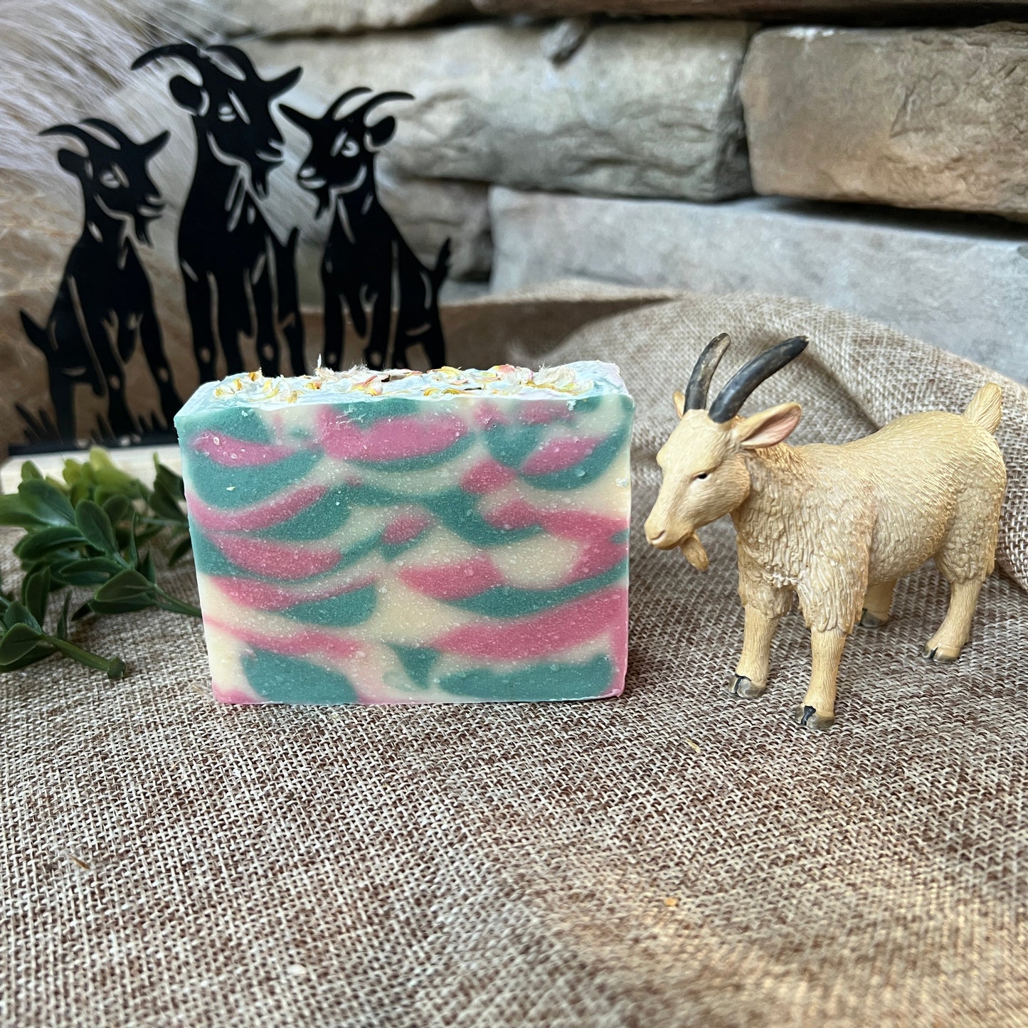 Colorful soap bar with a goat figurine and decorative metal goats on a textured surface.