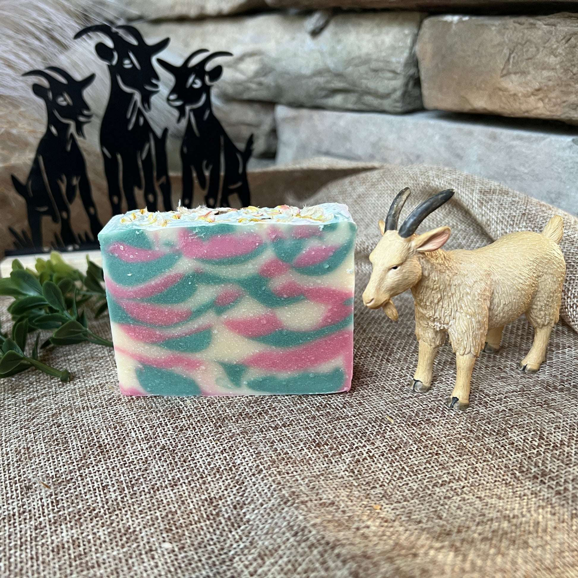 Colorful soap bar with a goat figurine and decorative metal goats on a textured surface.