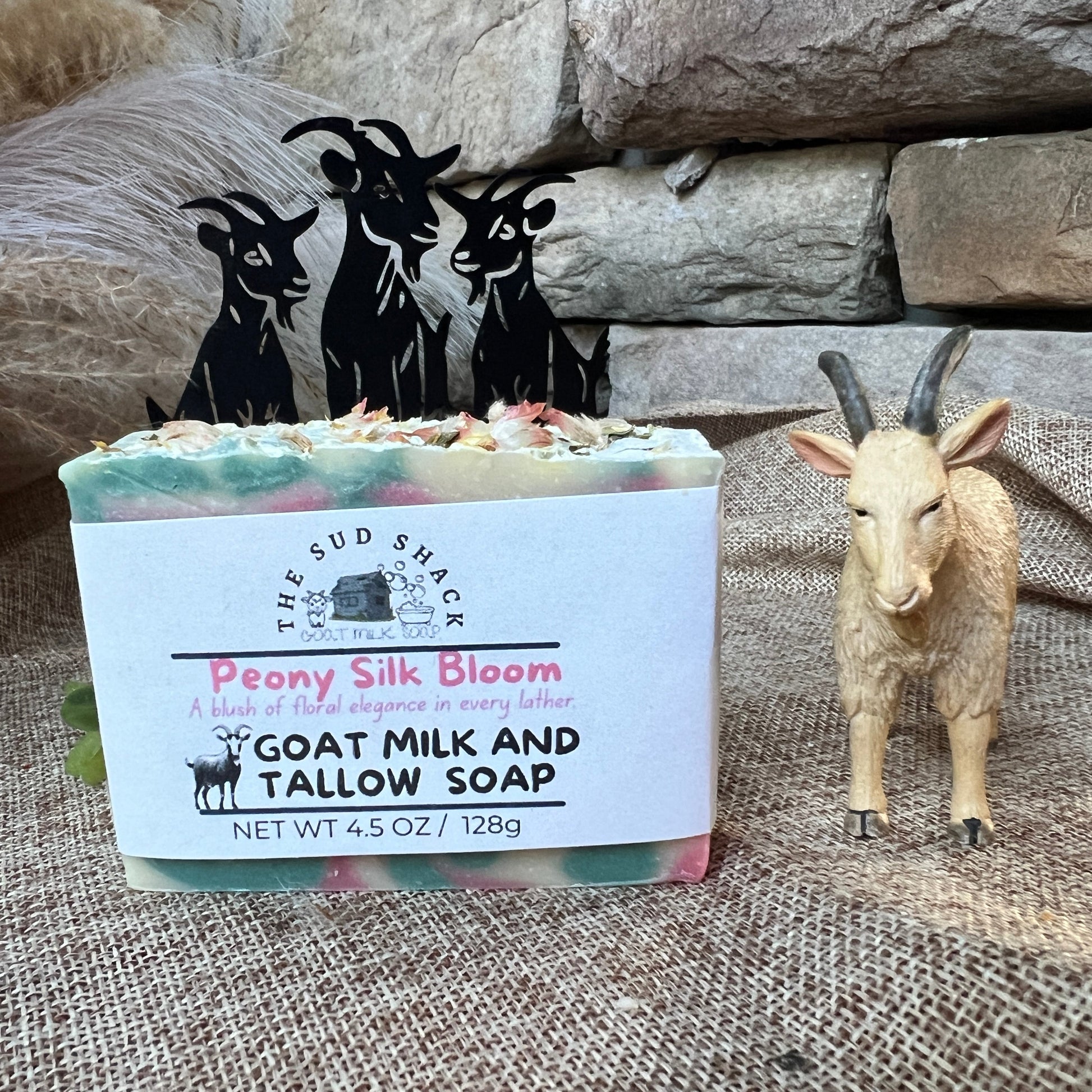 Bar of soap with a label featuring 'The Sud Shack' branding, surrounded by decorative goat figurines and a stone wall.