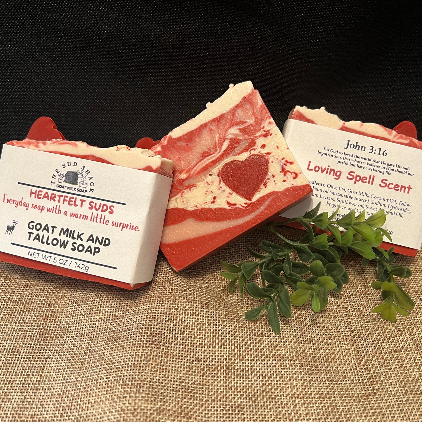 Three bars of soap with visible heart designs on a textured surface, accompanied by a small plant.