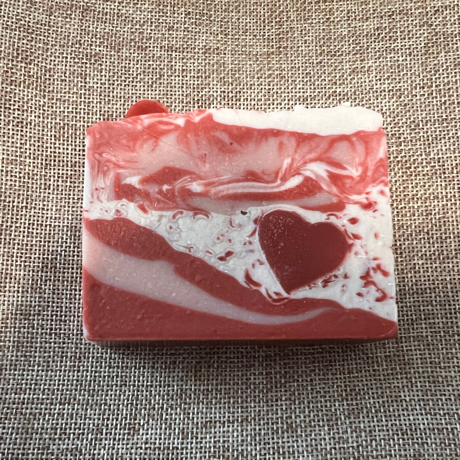Red and white swirled soap bar with a heart design on a textured fabric background