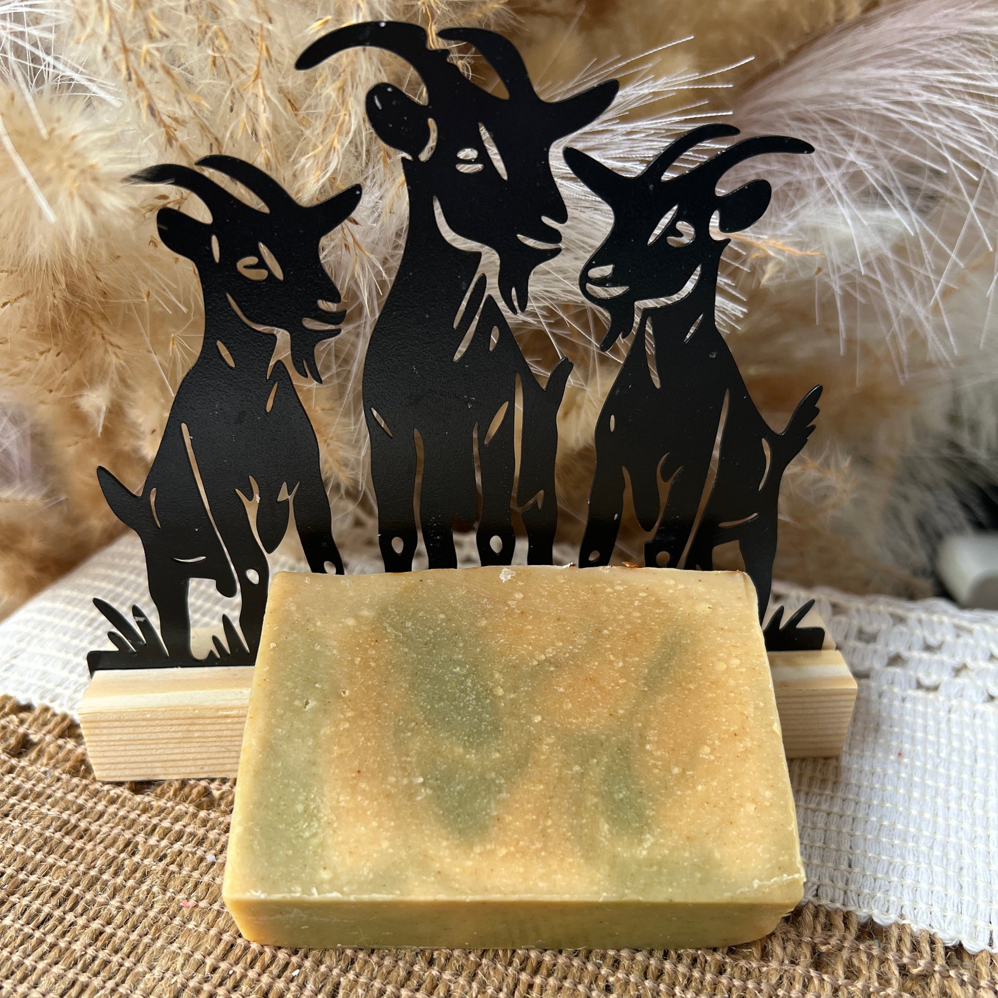 Bar of soap on a wooden block with black goat design in the background.