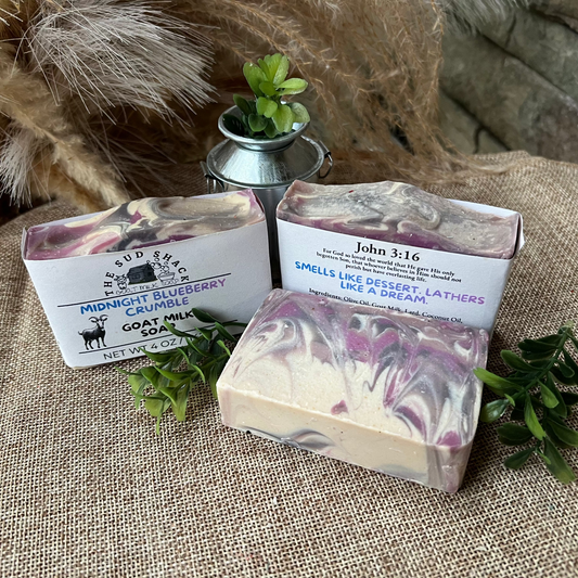 Three bars of soap with packaging on a textured surface with plants.