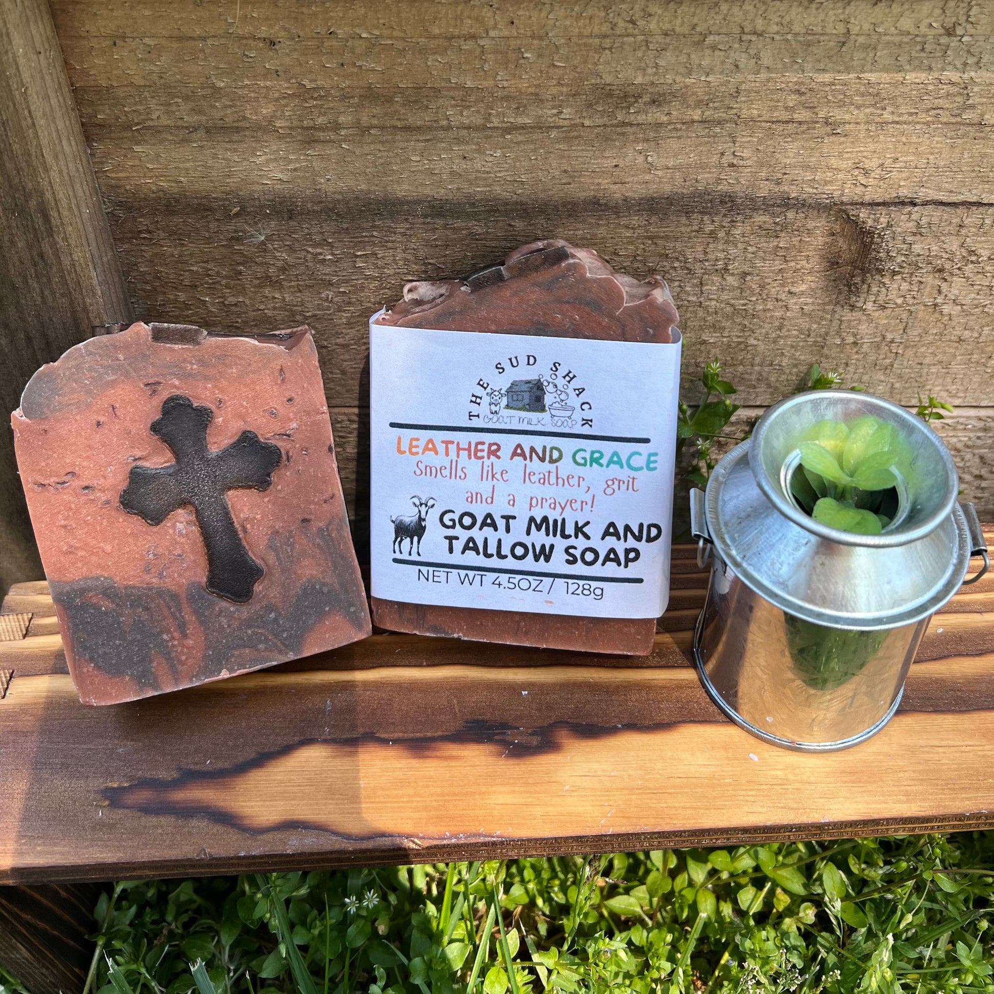 Two soap bars with labels on a wooden surface, one featuring a cross design.