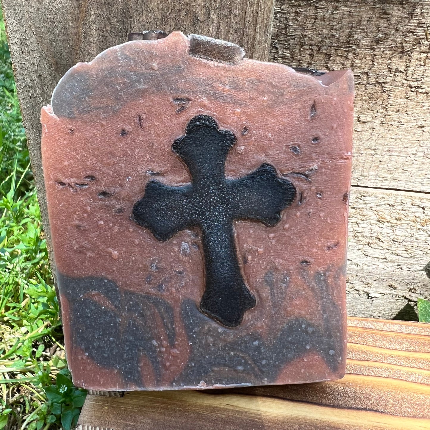 Bar of soap with a black cross design on a wooden surface