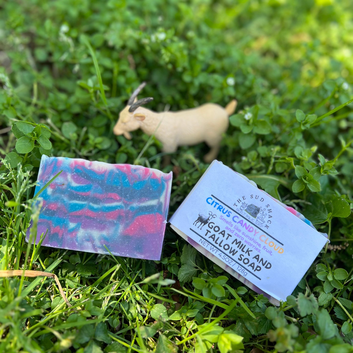 Bar of soap with a label on grass, with a goat in the background