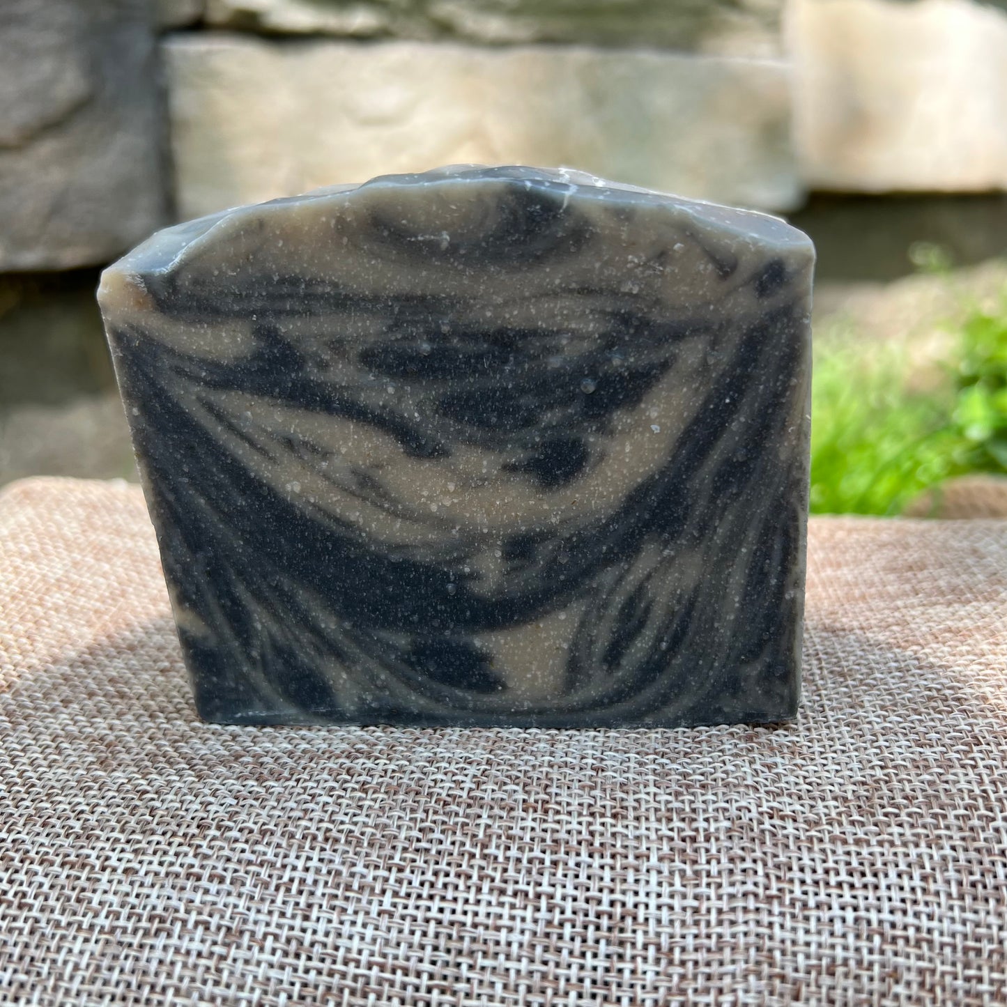 Bar of black and tan  soap on a textured surface with a natural stone background