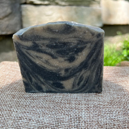 Bar of black and tan  soap on a textured surface with a natural stone background