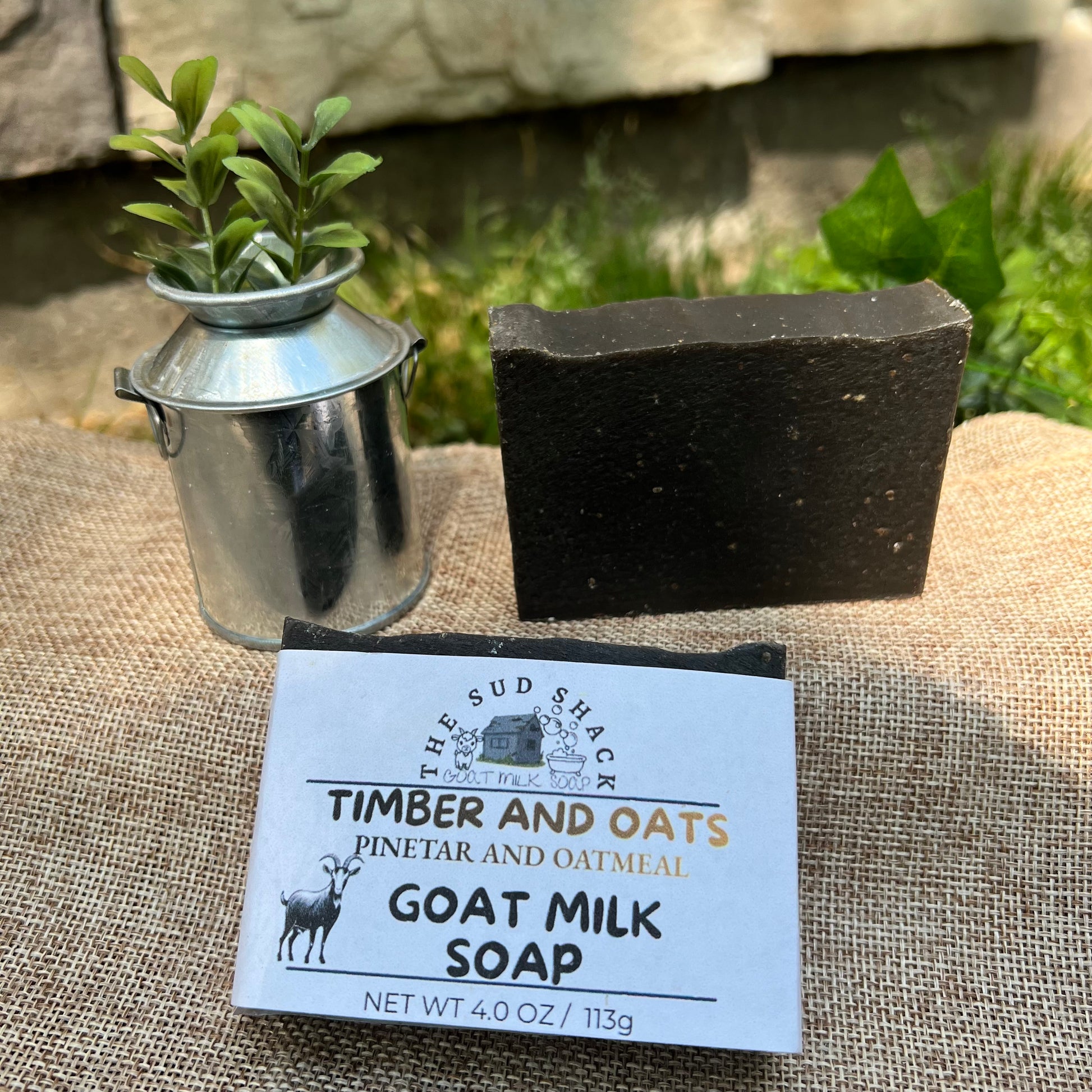 Goat milk soap bar with label on a textured surface, plant in the background