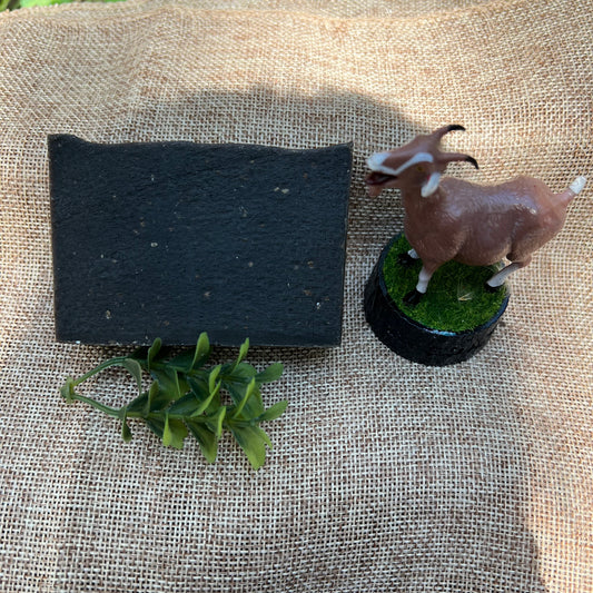 Small goat figurine with a black square and green leaves on a textured fabric background