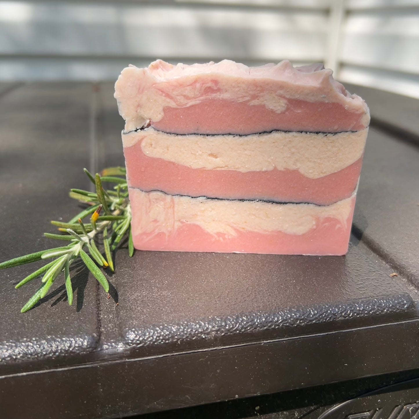 Pink layered soap bar with rosemary on a dark surface