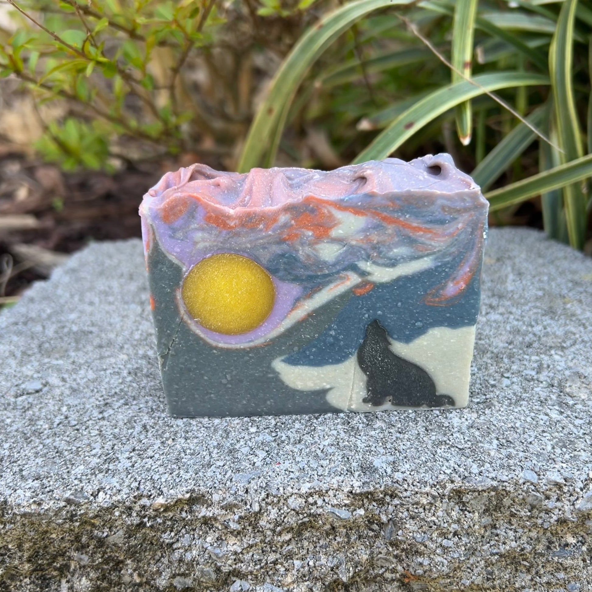 Soap bar with artistic design of a wolf and moon on a stone surface with plants in the background