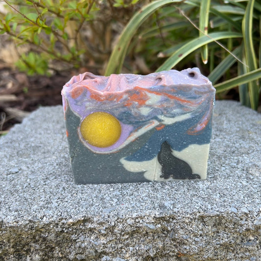 Soap bar with artistic design of a wolf and moon on a stone surface with plants in the background
