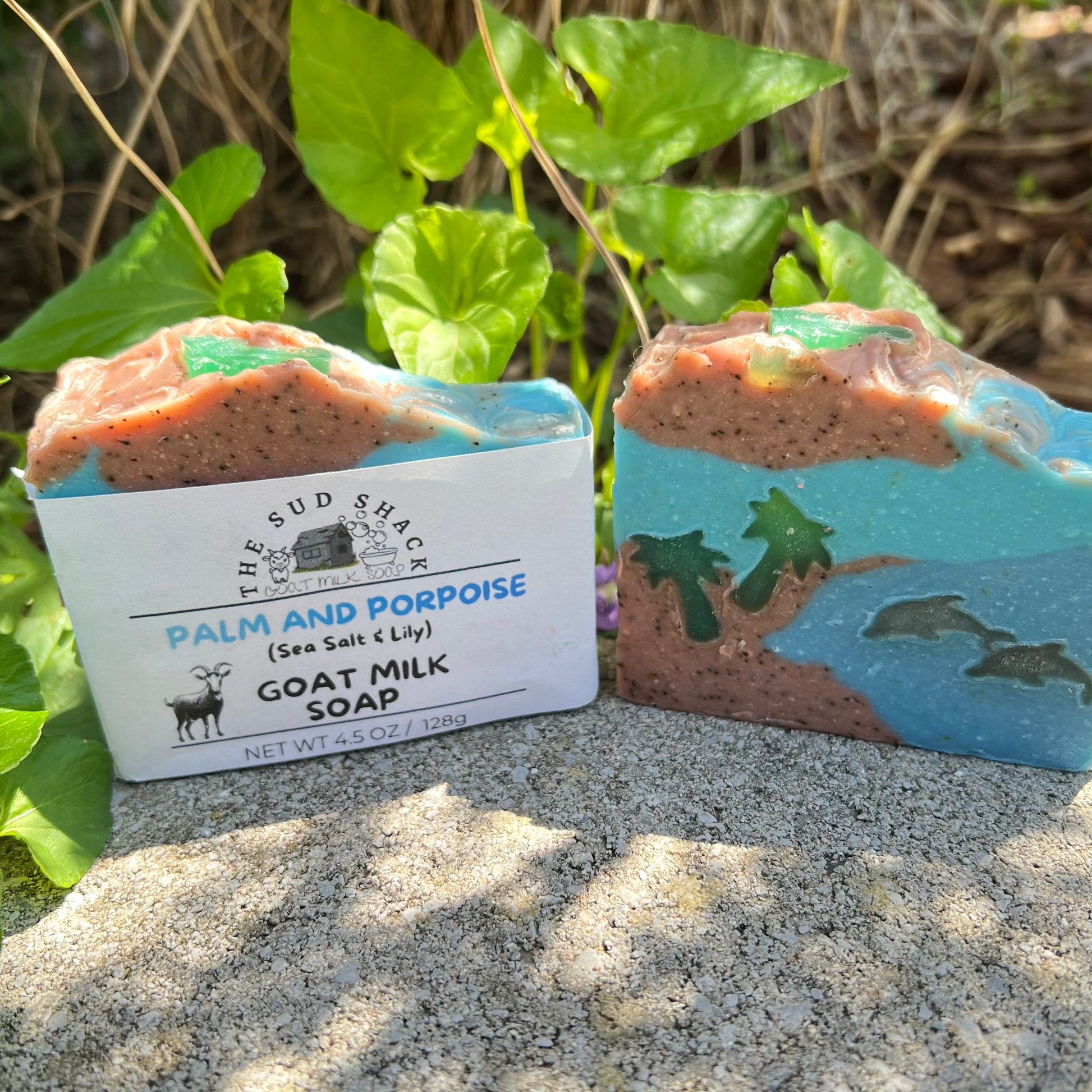 Goat milk soap with a label on a sandy surface with a dolphin and palm trees with greenery in the background