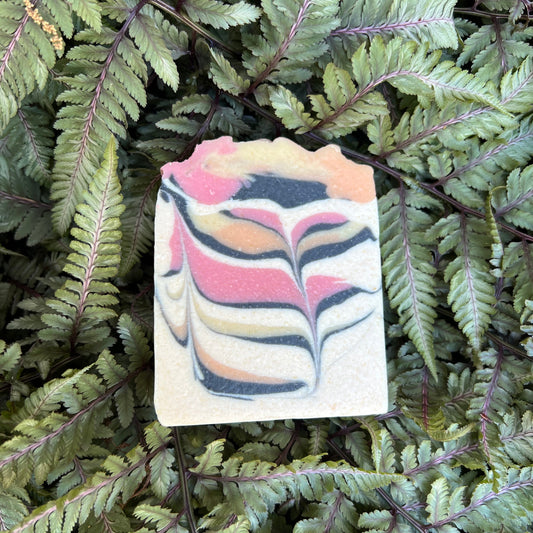 Colorful soap bar with a swirled pattern lying on green fern leaves