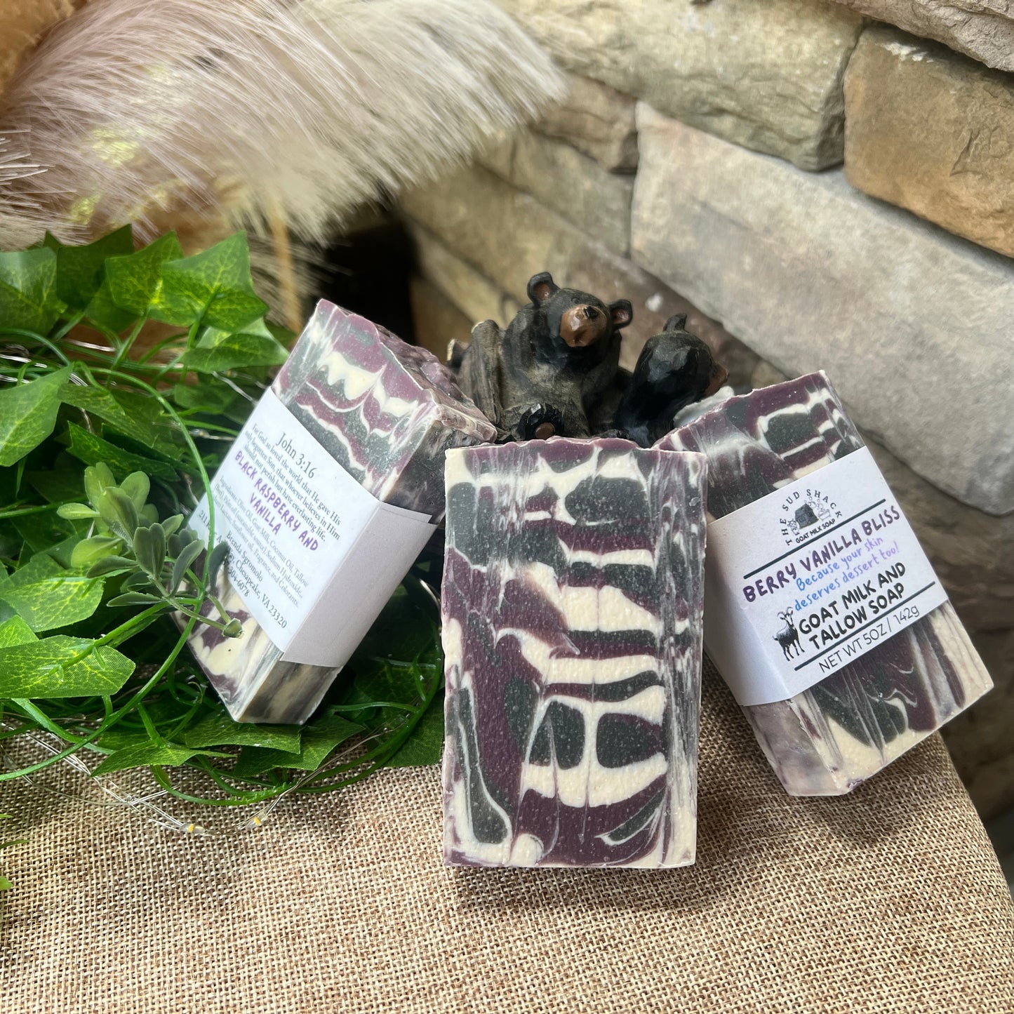 Three soap bars with packaging on a stone surface with greenery
