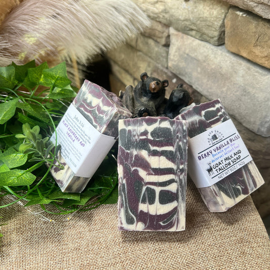 Three soap bars with packaging on a stone surface with greenery