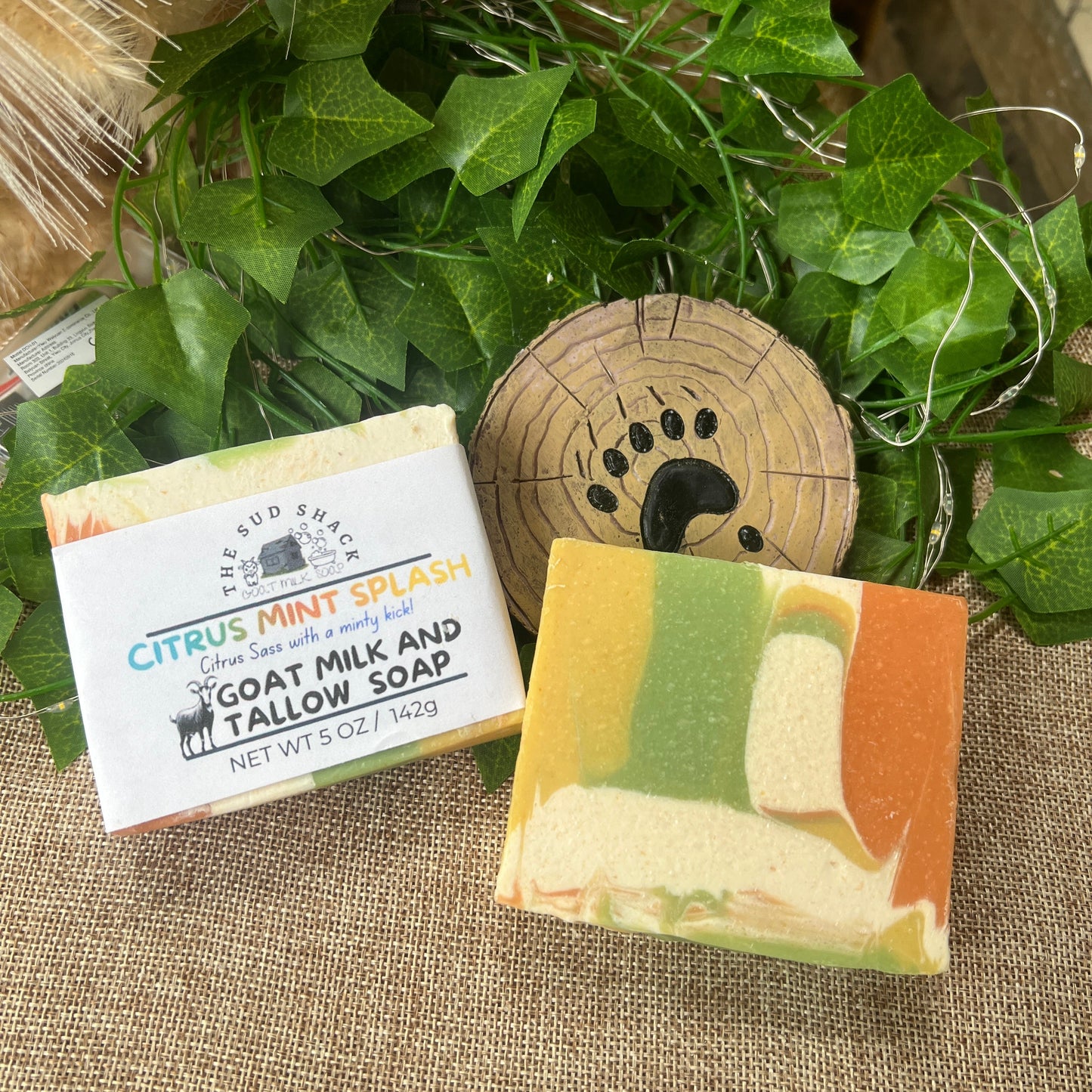 Two bars of soap with labels on a textured surface with greenery