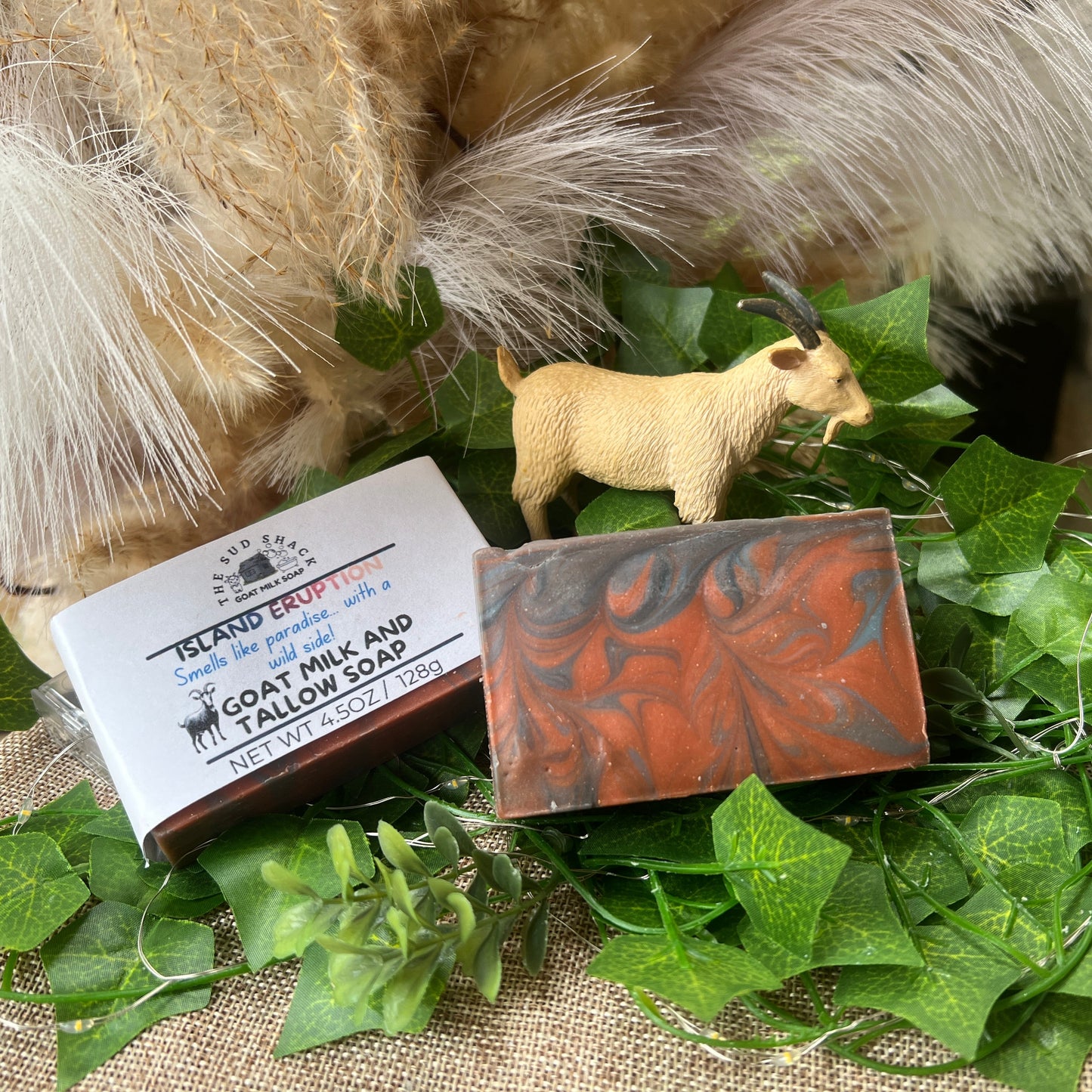 Two bars of soap with labels on a green leafy background with a goat figurine.