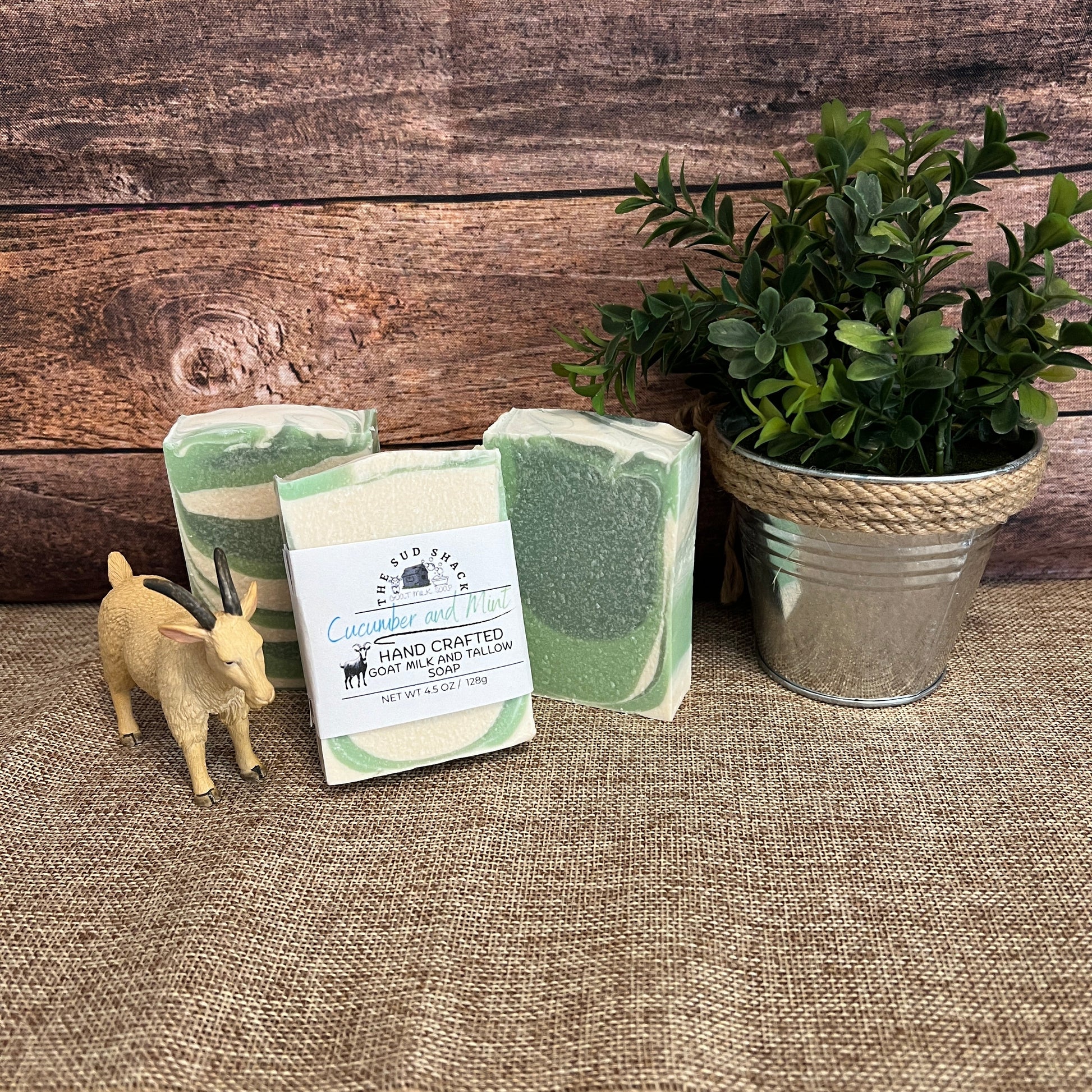Three green bars of soap with a plant and small figurine on a textured surface.