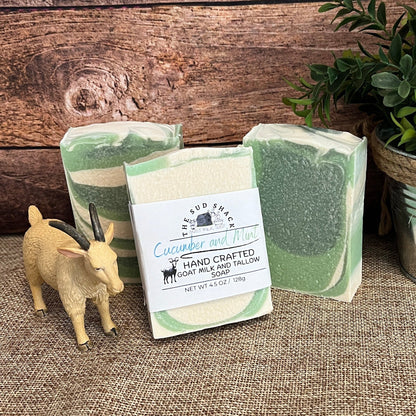 Three green bars of soap with a plant and small figurine on a textured surface.