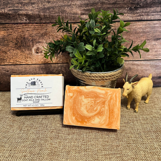 Handcrafted soap bar with packaging, potted plant, and toy goat on a textured surface with wooden background