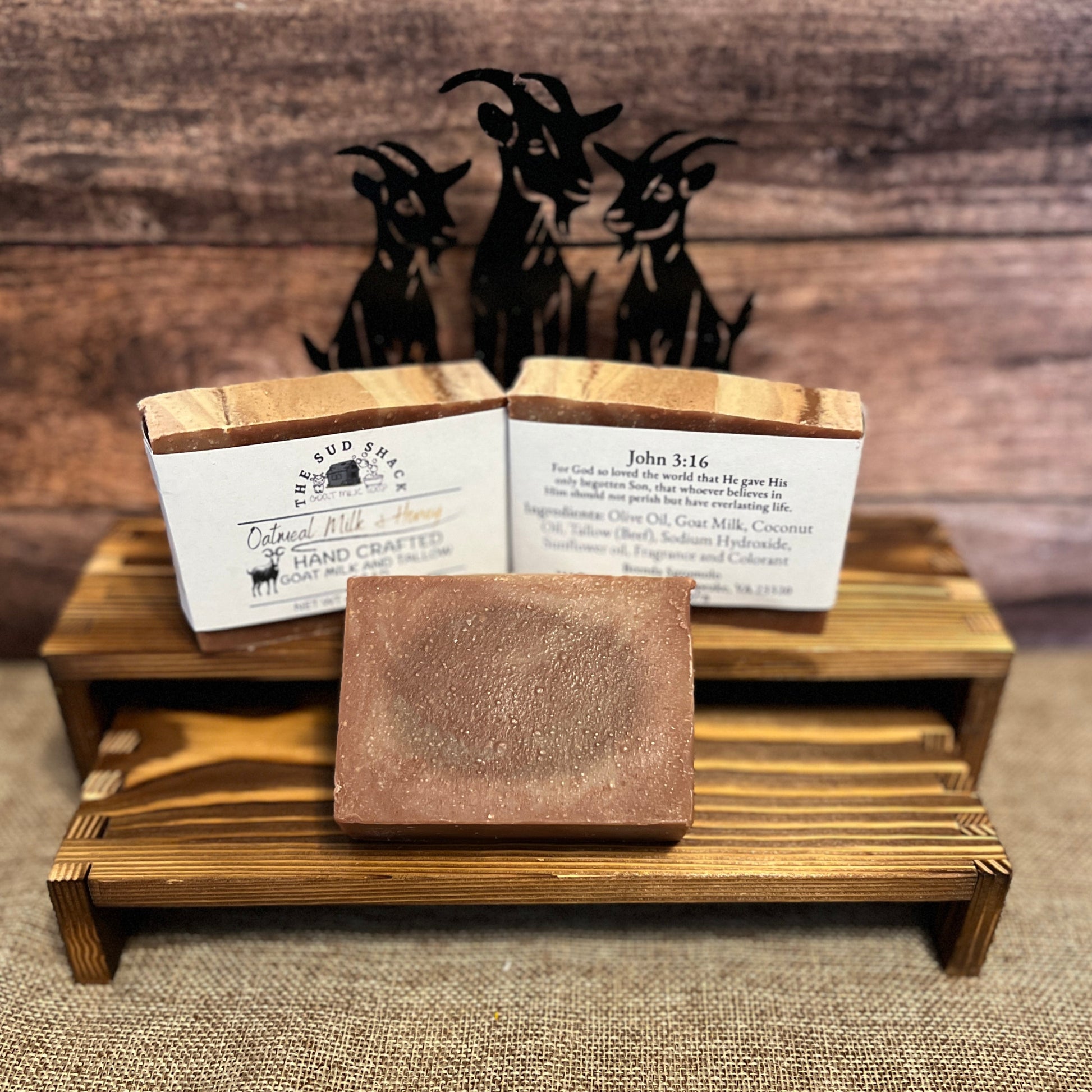 wooden stand with 3 bars of soap and figurine in the back with a rustic background.