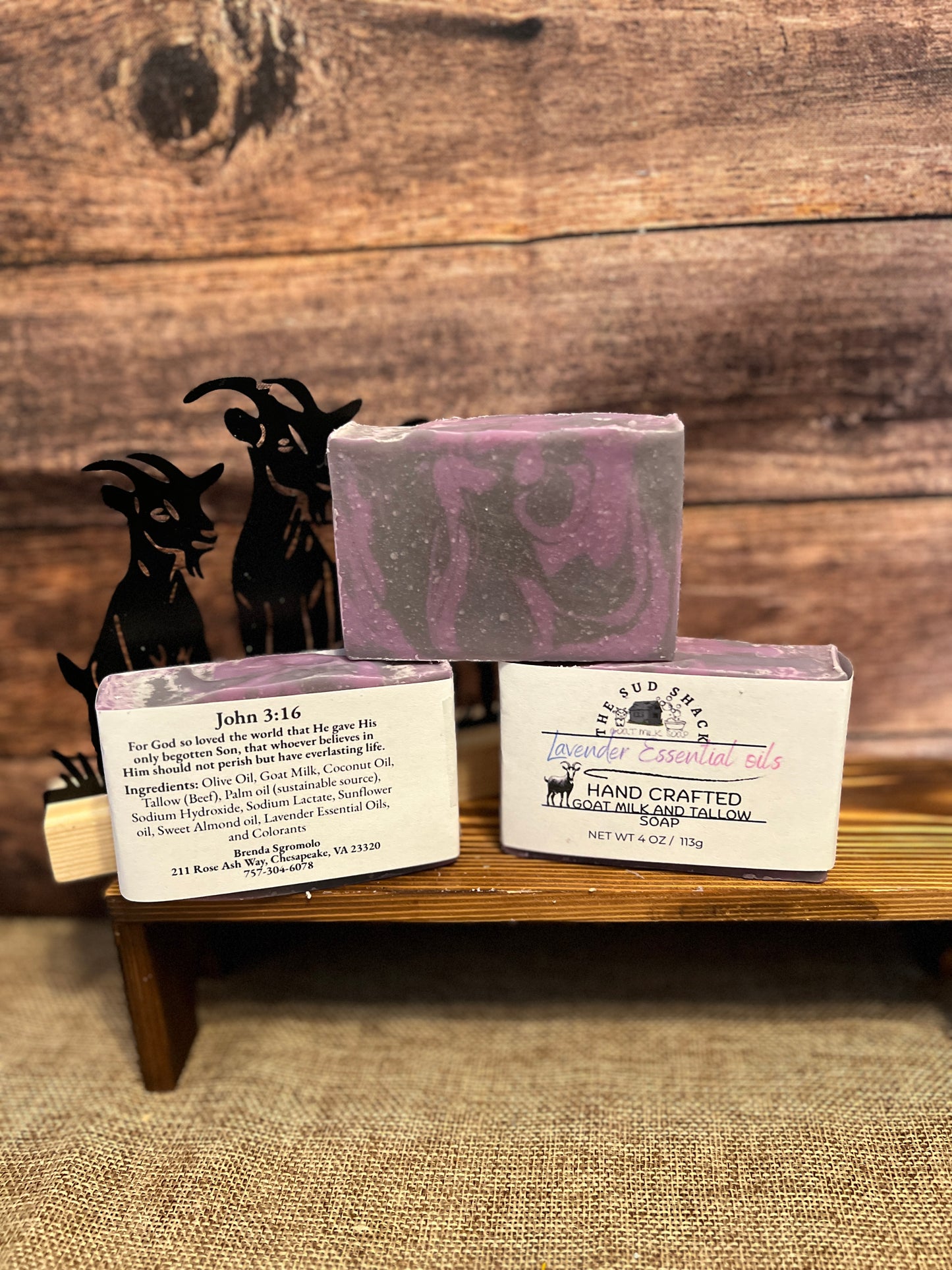 Three soap bars with labels on a wooden stand against a rustic wooden background