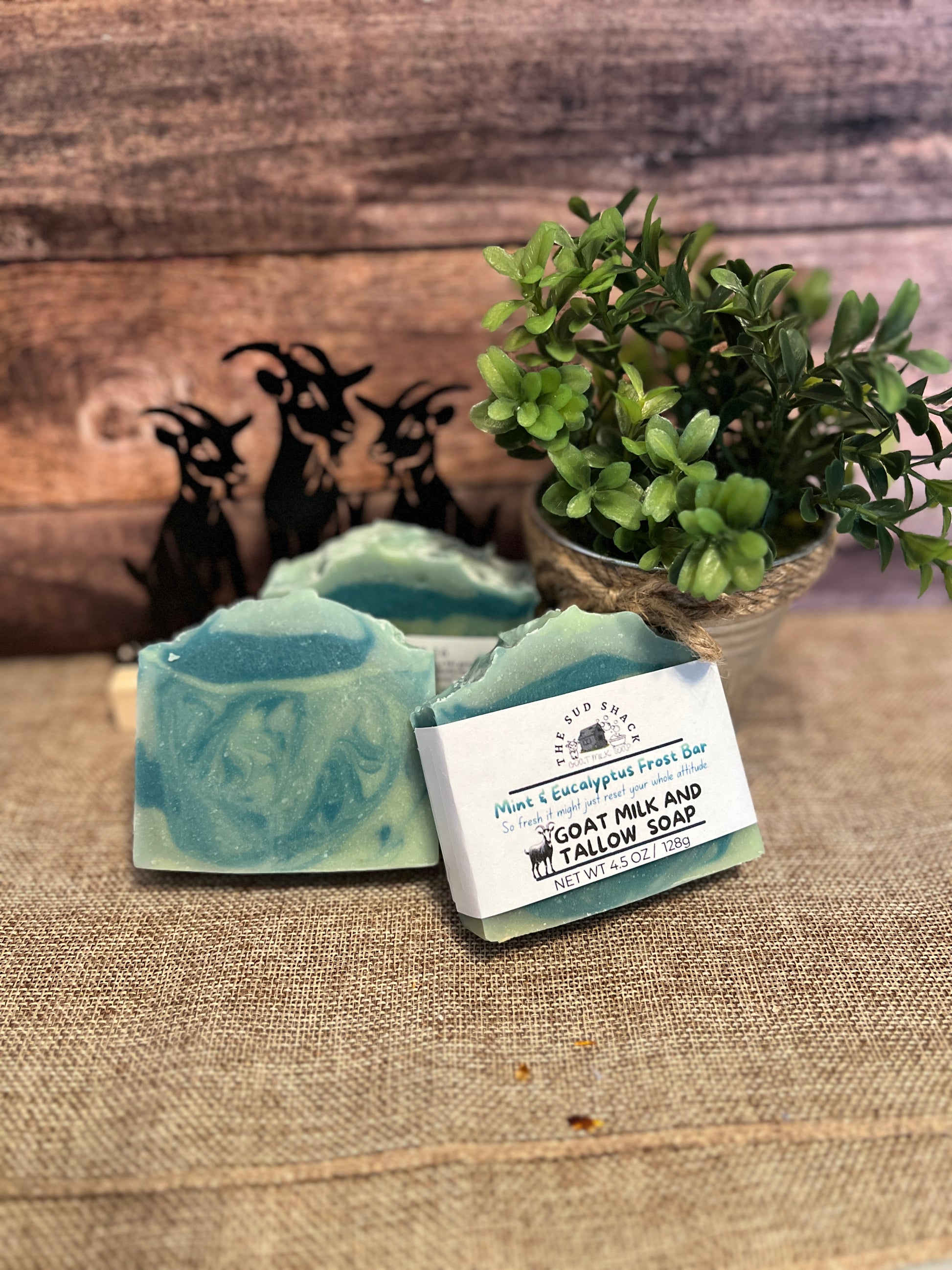 Green soap bar with a label on a textured surface with plants and figurines in the background