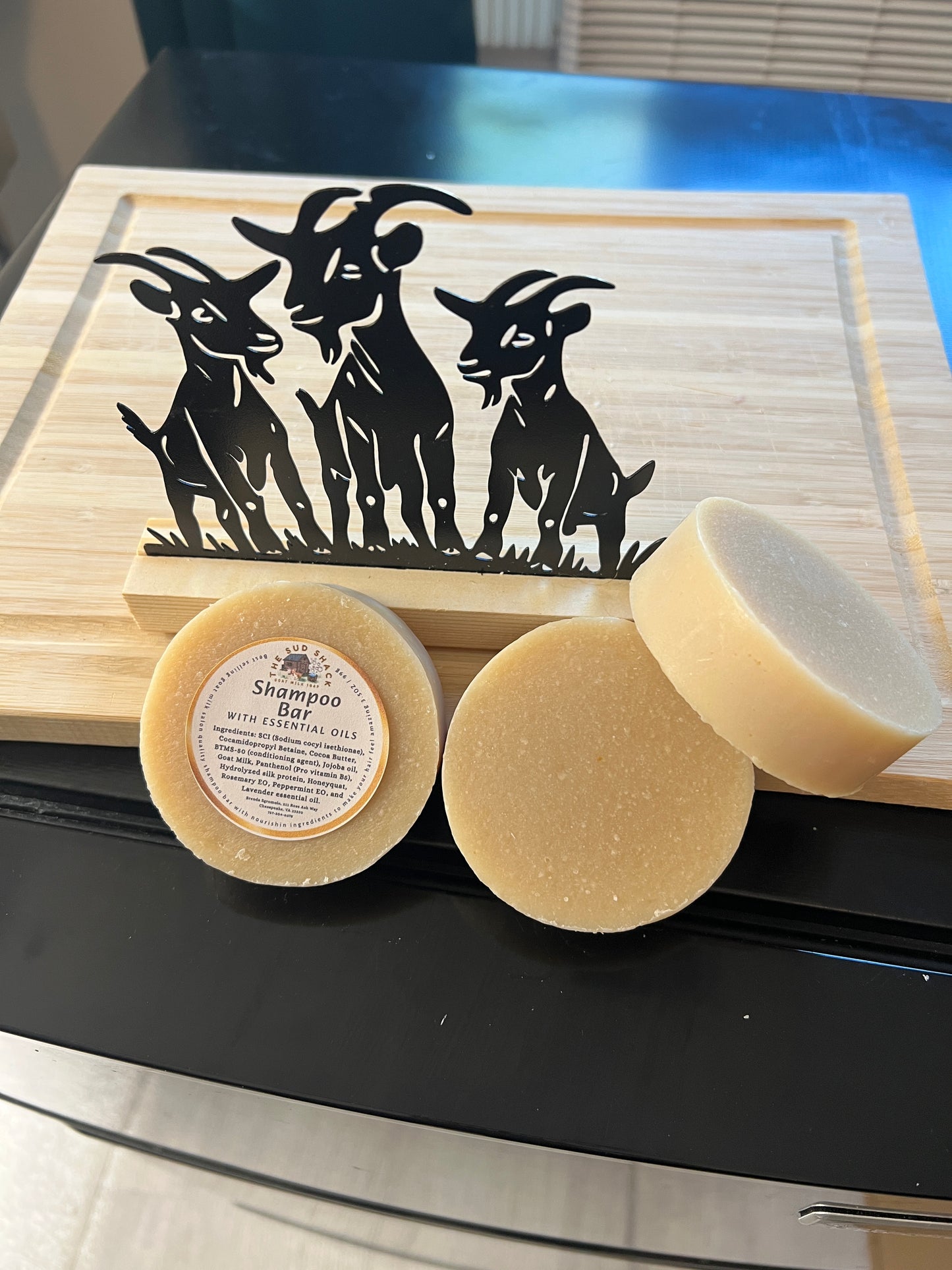 Three bars of soap on a wooden block with a black goat silhouette in the background.